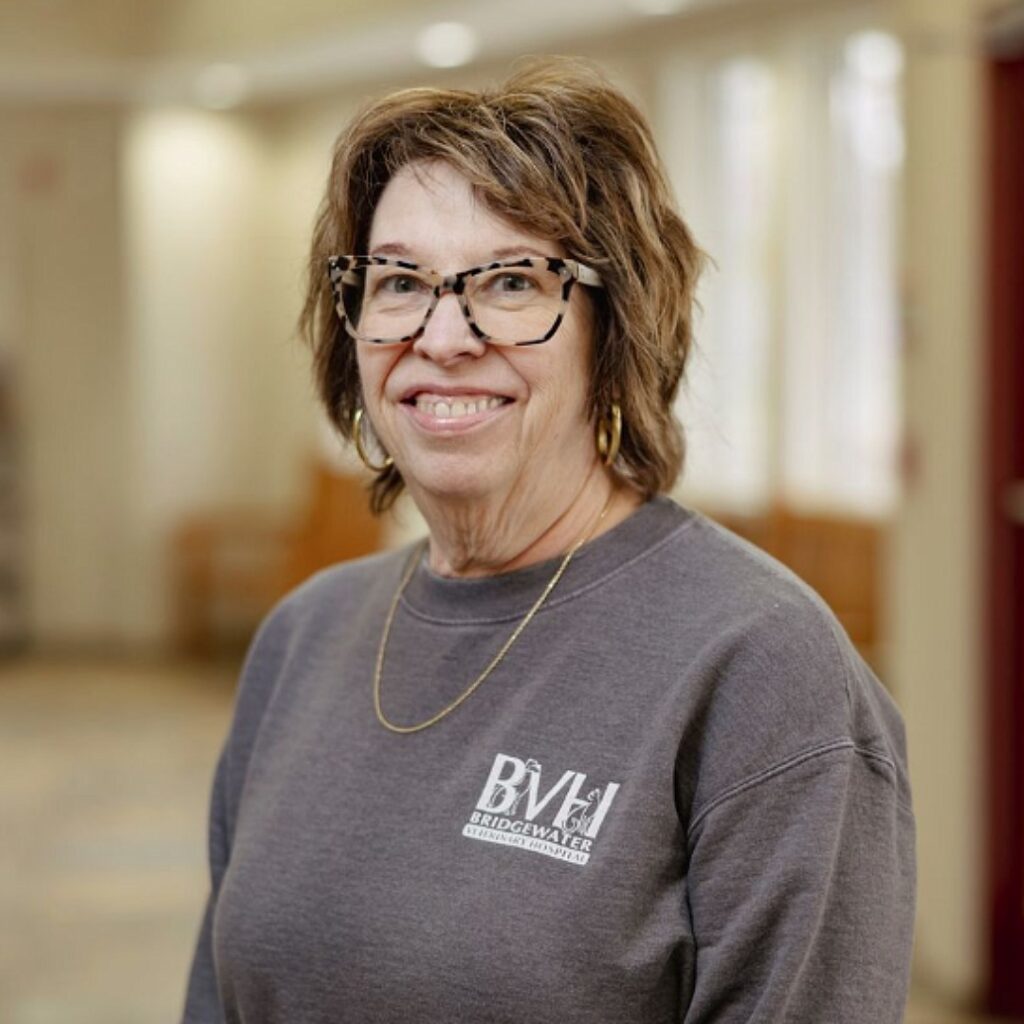 Donna-Receptionist, female with short brown hair wearing glasses and a long sleeved gray shirt