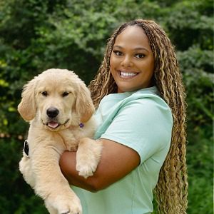 Female with long curly brown and blond hair holding a golden retriever puppy